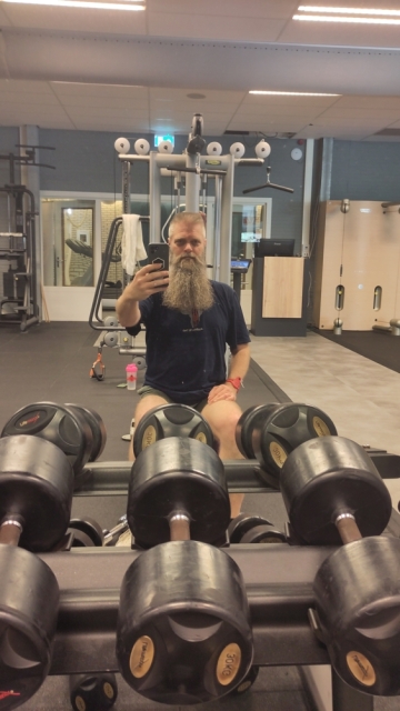 Selfie in de spiegel bij de fitness, grote gewichten op de voorgrond.
