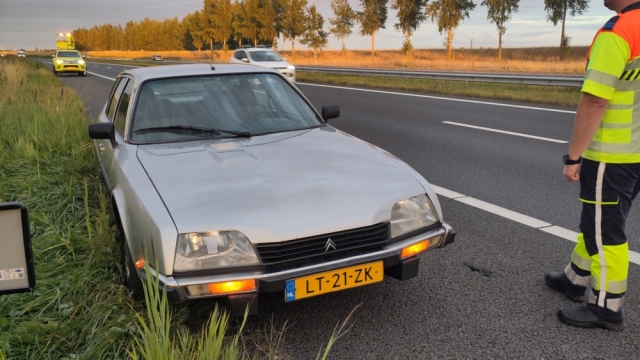  Zilvergrijze Citroën CX op de vluchtstrook, noodknipperlichten aan. Achter de CX staat een auto van Rijkswaterstaat, de bestuurder daarvan staat rechts in beeld.