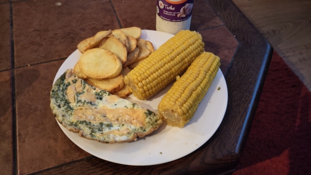Bord met omelet, goudbruin gebakken aardappels en 2 maïskolven